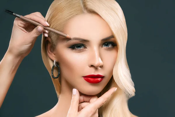 Beautiful blonde woman applying eyebrow makeup, isolated on grey — Stock Photo