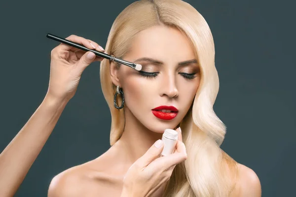 Hermosa mujer rubia aplicando maquillaje glamoroso con sombras de ojos, aislado en gris - foto de stock