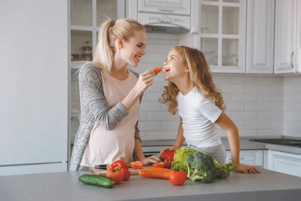 Smiling pregnant mother giving daughter piece of bell pepper — Stock Photo