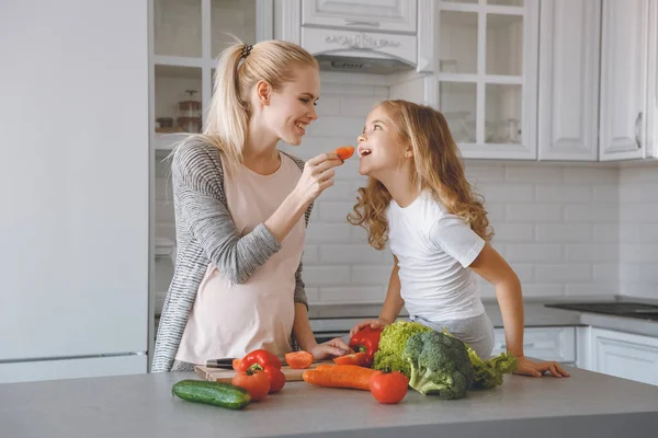 Sonriente embarazada madre dando hija pedazo de pimiento - foto de stock