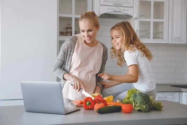 Pregnant mother and daughter cooking together and looking at laptop — Stock Photo