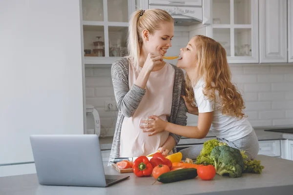 Sonriente embarazada madre dando hija pedazo de pimiento - foto de stock