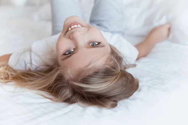 Lächelndes Kind, das auf dem Rücken auf dem Bett liegt und in die Kamera schaut — Stockfoto