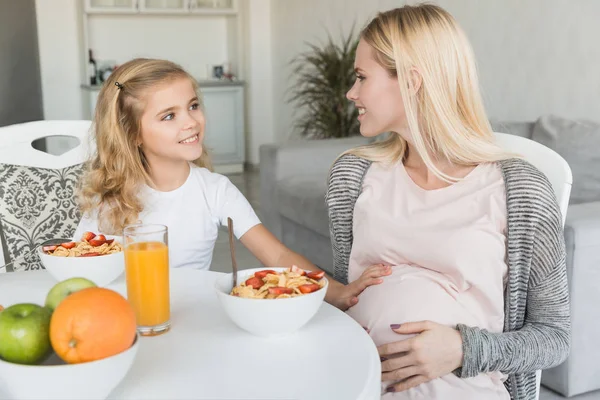 Sonriente hija tocando embarazada madre vientre - foto de stock