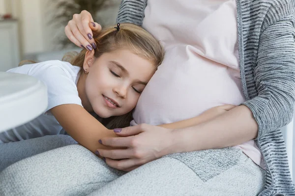 Imagen recortada de hija alegre durmiendo en el vientre de la madre embarazada - foto de stock