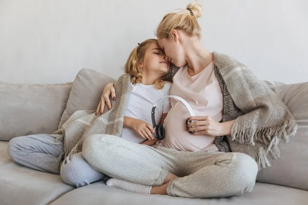 Madre embarazada e hija dando a escuchar música al feto - foto de stock
