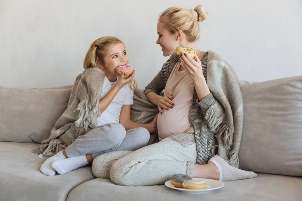 Happy pregnant mother and daughter eating donuts — Stock Photo