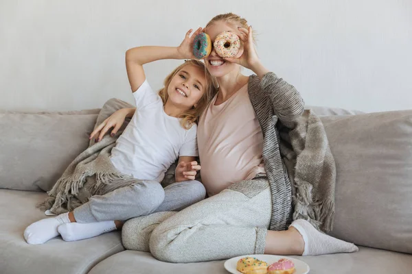 Happy pregnant mother and daughter covering eyes with donuts — Stock Photo