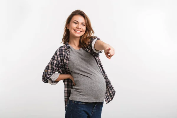 Sorridente donna incinta che punta lontano isolato su grigio — Foto stock