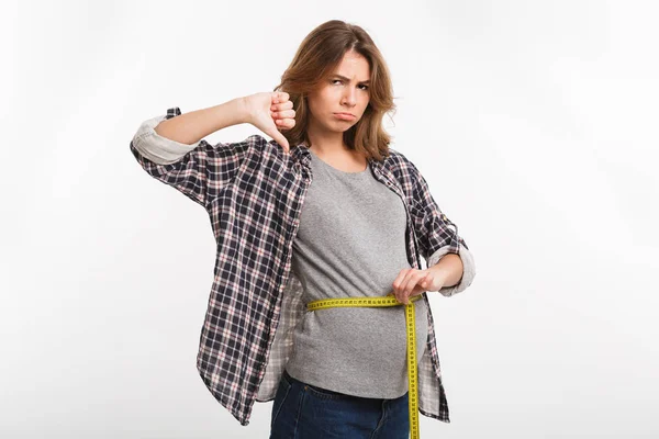 Pregnant woman with measuring tape on tummy showing thumb down isolated on grey — Stock Photo