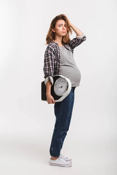 Bouleversé femme enceinte tenant des balances et regardant la caméra isolée sur blanc — Photo de stock