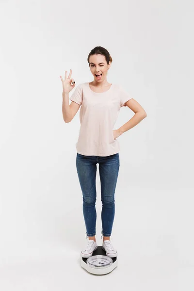 Молодая женщина показывает хорошо знак, стоя на весах изолированы на белом — стоковое фото