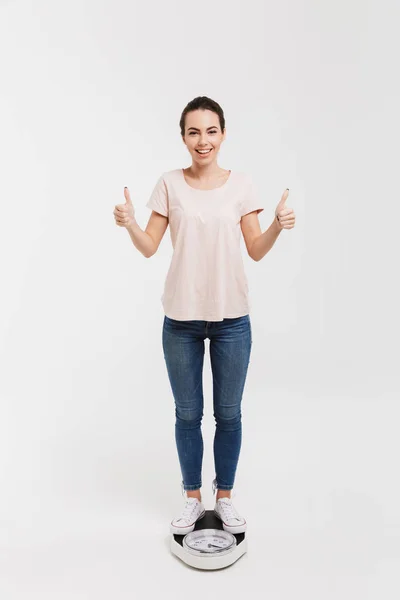 Mujer joven mostrando los pulgares hacia arriba mientras está de pie en escamas aisladas en blanco - foto de stock