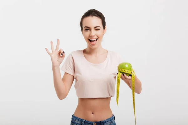Woman holding apple tied with measuring tape and showing okay sign isolated on white — Stock Photo