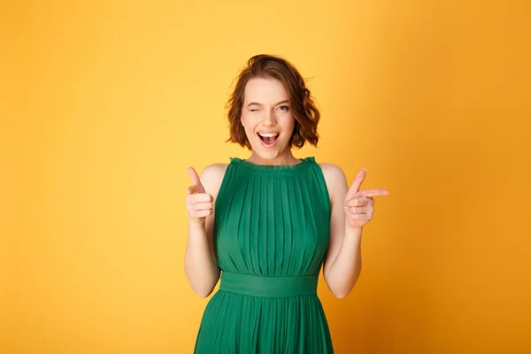 Portrait of winking woman pointing at camera isolated on orange — Stock Photo