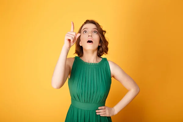 Portrait of young emotional woman akimbo pointing up isolated on orange — Stock Photo