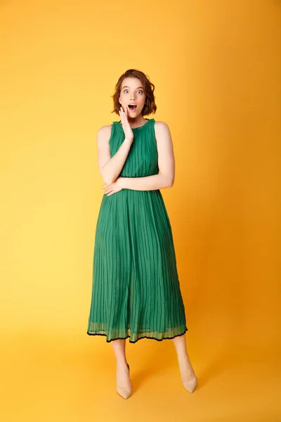 Beautiful surprised woman in green dress looking at camera isolated on orange — Stock Photo