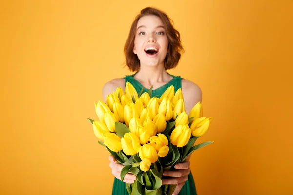 Foco selectivo de mujer feliz que presenta ramo de tulipanes amarillos de primavera en manos aisladas en naranja - foto de stock