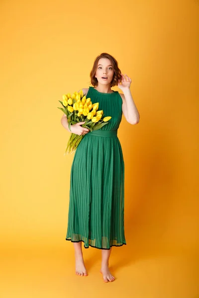 Красива молода жінка в зеленій сукні з букетом жовтих тюльпанів ізольована на апельсині — стокове фото