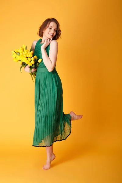 Belle jeune femme en robe avec bouquet de tulipes printanières isolées sur orange — Photo de stock
