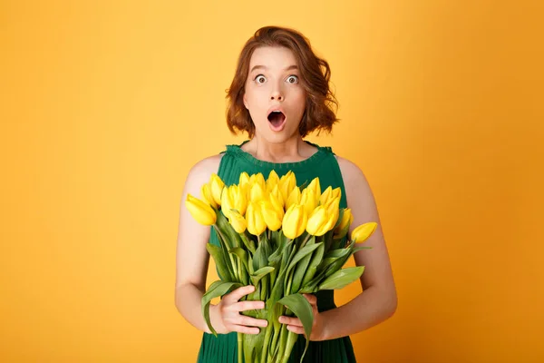 Portrait of shocked woman with bouquet of yellow tulips isolated on orange — Stock Photo