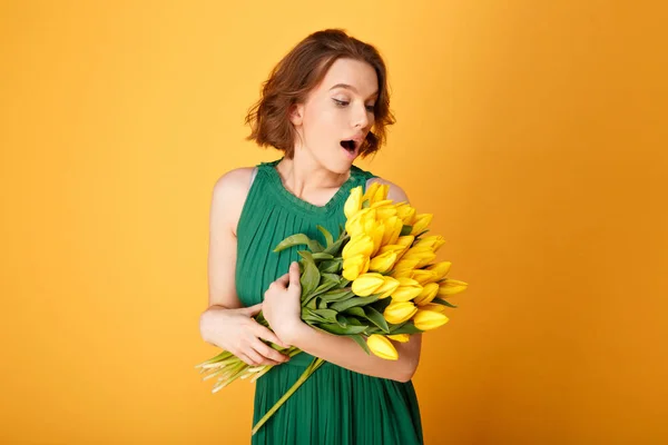 Portrait de femme surprise regardant un bouquet de tulipes jaunes isolées sur orange — Photo de stock