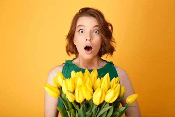 Retrato de mulher chocada com buquê de tulipas amarelas olhando para câmera isolada em laranja — Fotografia de Stock