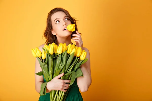 Ritratto di donna pensierosa con tulipano in bocca e bouquet di tulipani gialli isolati su arancione — Foto stock