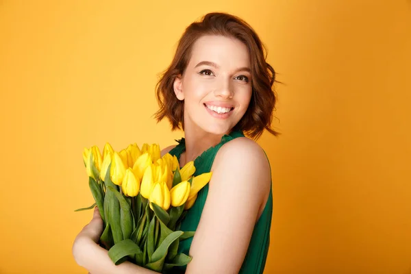 Портрет счастливой женщины с букетом желтых тюльпанов, изолированных на оранжевом — стоковое фото