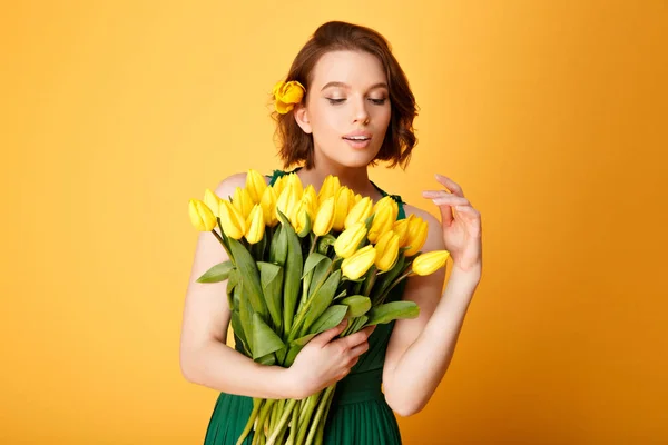 Портрет молодой женщины, смотрящей на букет желтых тюльпанов в руке, изолированных на оранжевом — стоковое фото