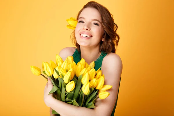 Portrait of cheerful woman with bouquet of yellow tulips isolated on orange — Stock Photo