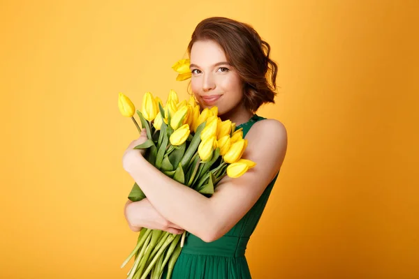 Retrato de mulher atraente com buquê de tulipas amarelas em mãos isoladas em laranja — Fotografia de Stock