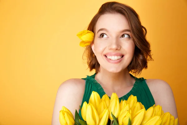Portrait of dreamy woman with bouquet of yellow tulips isolated on orange — Stock Photo