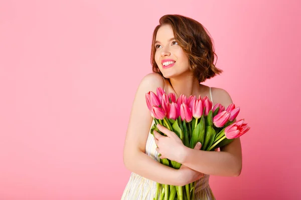 Mujer alegre con ramo de tulipanes rosados mirando hacia otro lado aislado en rosa - foto de stock