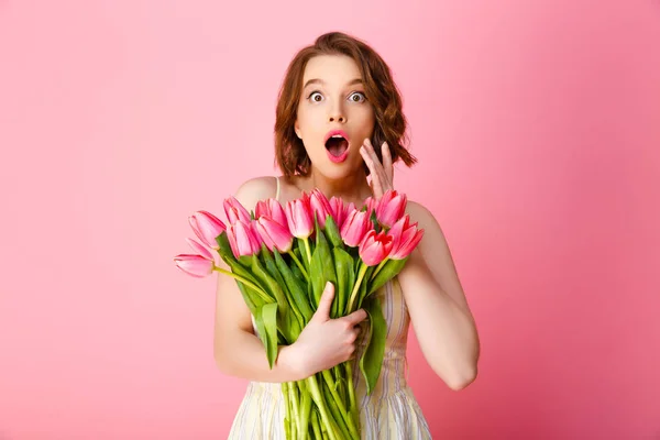 Retrato de mulher surpreso com buquê de tulipas primavera olhando para câmera isolada em rosa — Fotografia de Stock