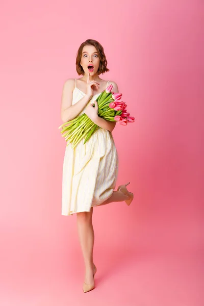 Jeune femme choquée avec bouquet de tulipes roses isolées sur rose — Photo de stock