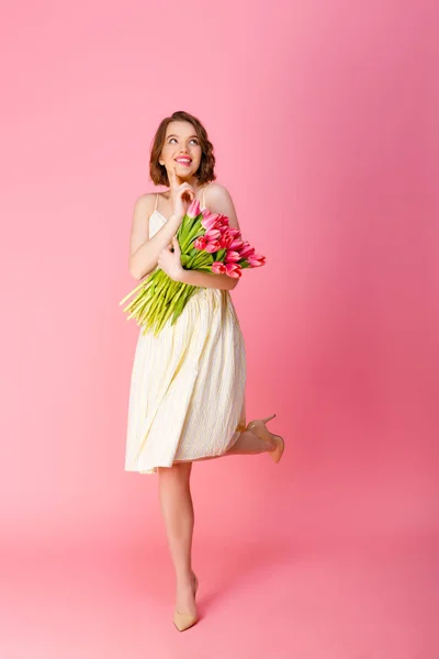 Femme rêveuse avec bouquet de tulipes roses isolées sur rose — Photo de stock
