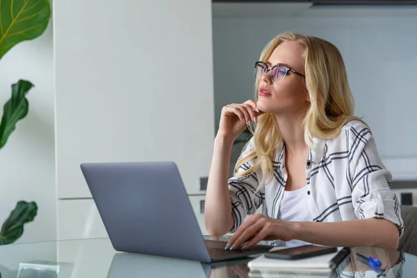 Schöne nachdenkliche blonde Frau mit Laptop während der Arbeit zu Hause — Stockfoto