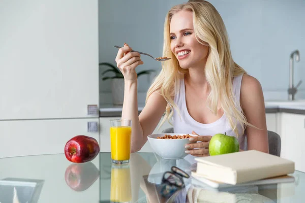 Beautiful happy young woman eating muesli for breakfast and looking away at home — Stock Photo