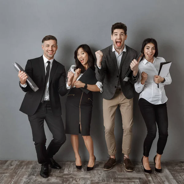 Gente de negocios multicultural feliz con carpetas y cuadernos de pie en la pared gris - foto de stock