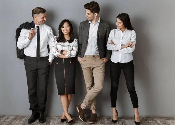 Smiling multicultural business people in formal wear standing at grey wall — Stock Photo