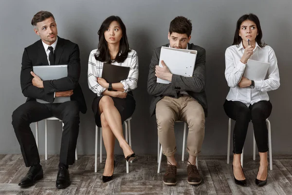 Gente de negocios multicultural asustada y pensativa con carpetas y cuadernos esperando una entrevista de trabajo - foto de stock