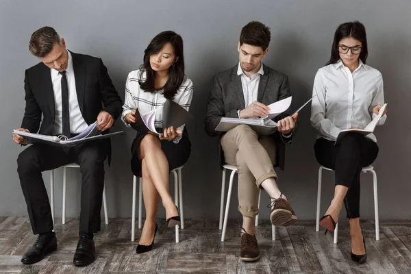 Personas de negocios multiculturales concentrados con carpetas y cuadernos a la espera de entrevista de trabajo - foto de stock