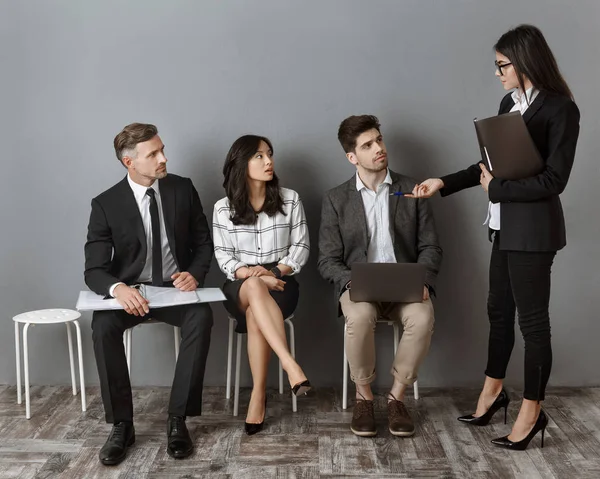 Empresaria elegir uno de los colegas para la entrevista de trabajo en se sienta contra la pared gris - foto de stock