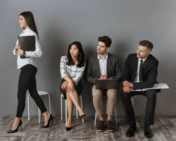 Smiling caucasian businesswoman going for job interview while multiethnic colleagues looking at her on chairs — Stock Photo