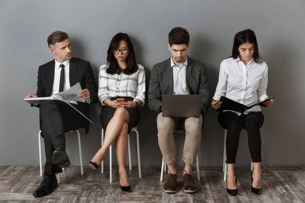 Pessoas de negócios multiétnicos com dispositivos digitais e pastas à espera de entrevista de emprego — Fotografia de Stock
