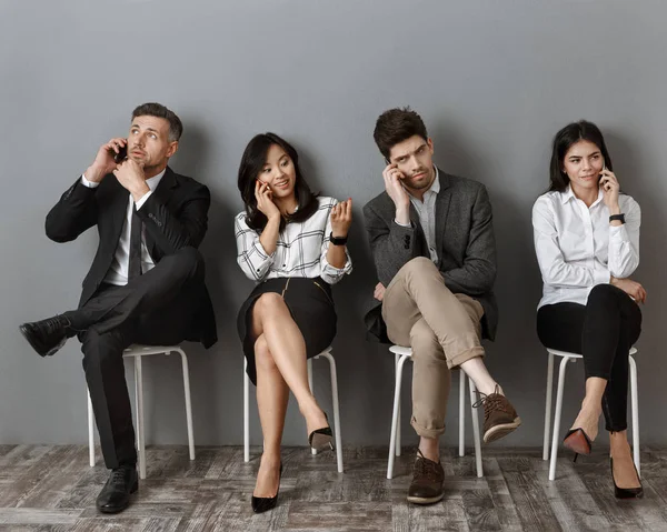 Gente de negocios interracial hablando en teléfonos inteligentes mientras espera entrevista de trabajo - foto de stock