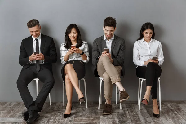 Sonriendo gente de negocios interracial usando teléfonos inteligentes mientras espera entrevista de trabajo - foto de stock