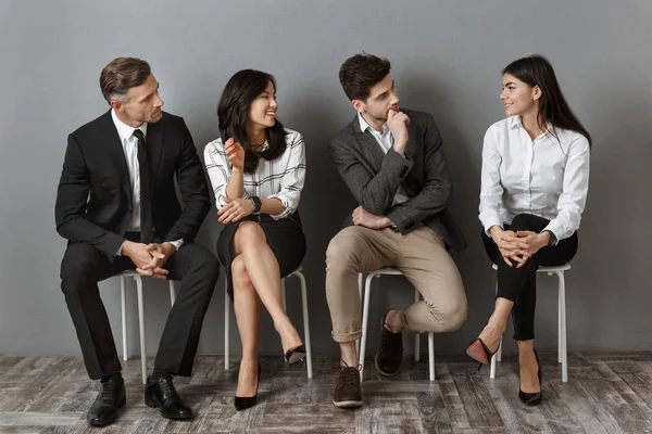 Gente de negocios interracial en ropa formal teniendo conversación mientras esperan entrevista de trabajo - foto de stock