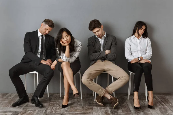 Pessoas de negócios inter-raciais cansadas em uso formal dormindo em cadeiras enquanto espera por entrevista de emprego — Fotografia de Stock